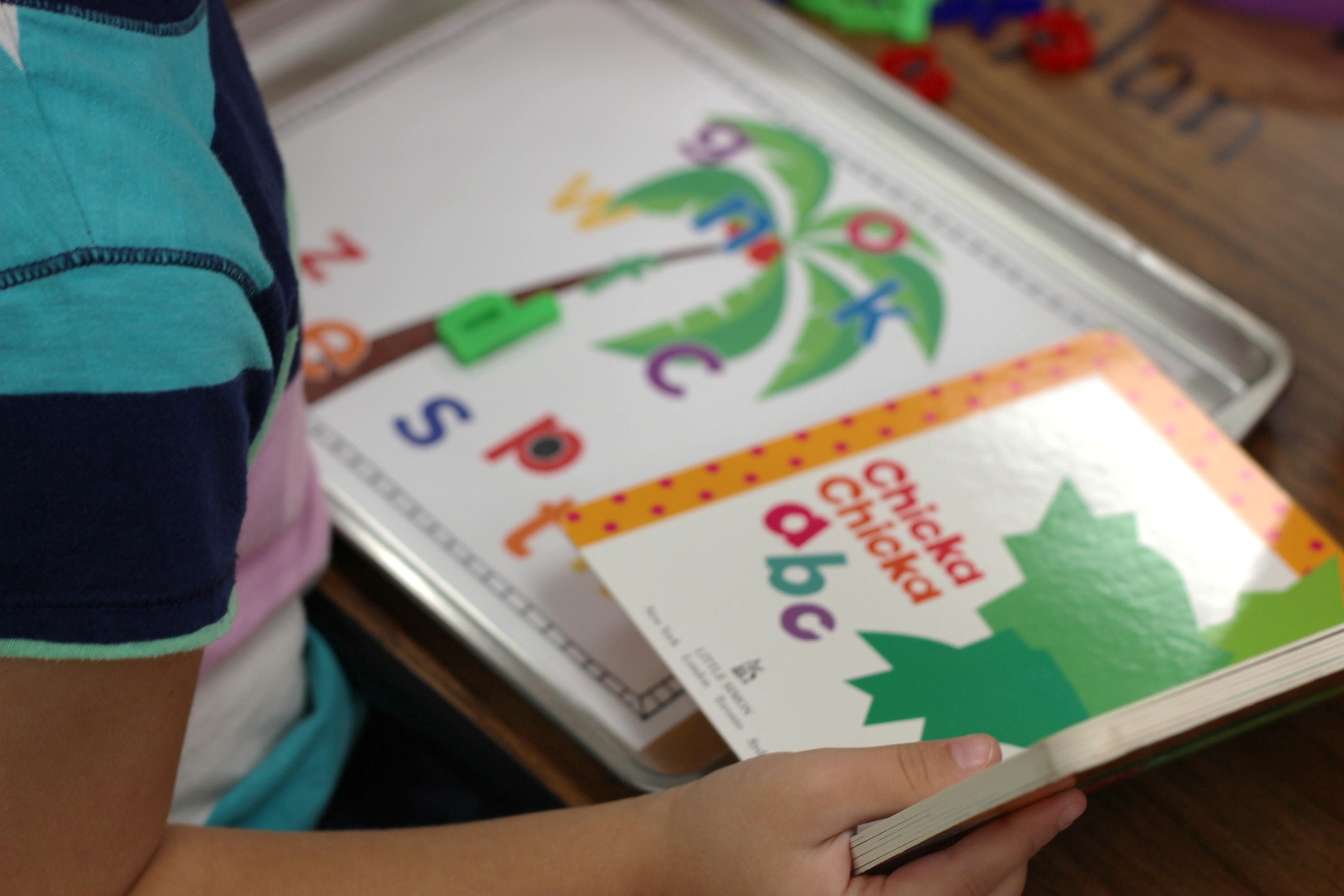 Child practicing alphabet letter recognition with a Chicka Chicka Boom Boom inspired ABC center, colorful letter manipulatives, and a children’s alphabet book.
