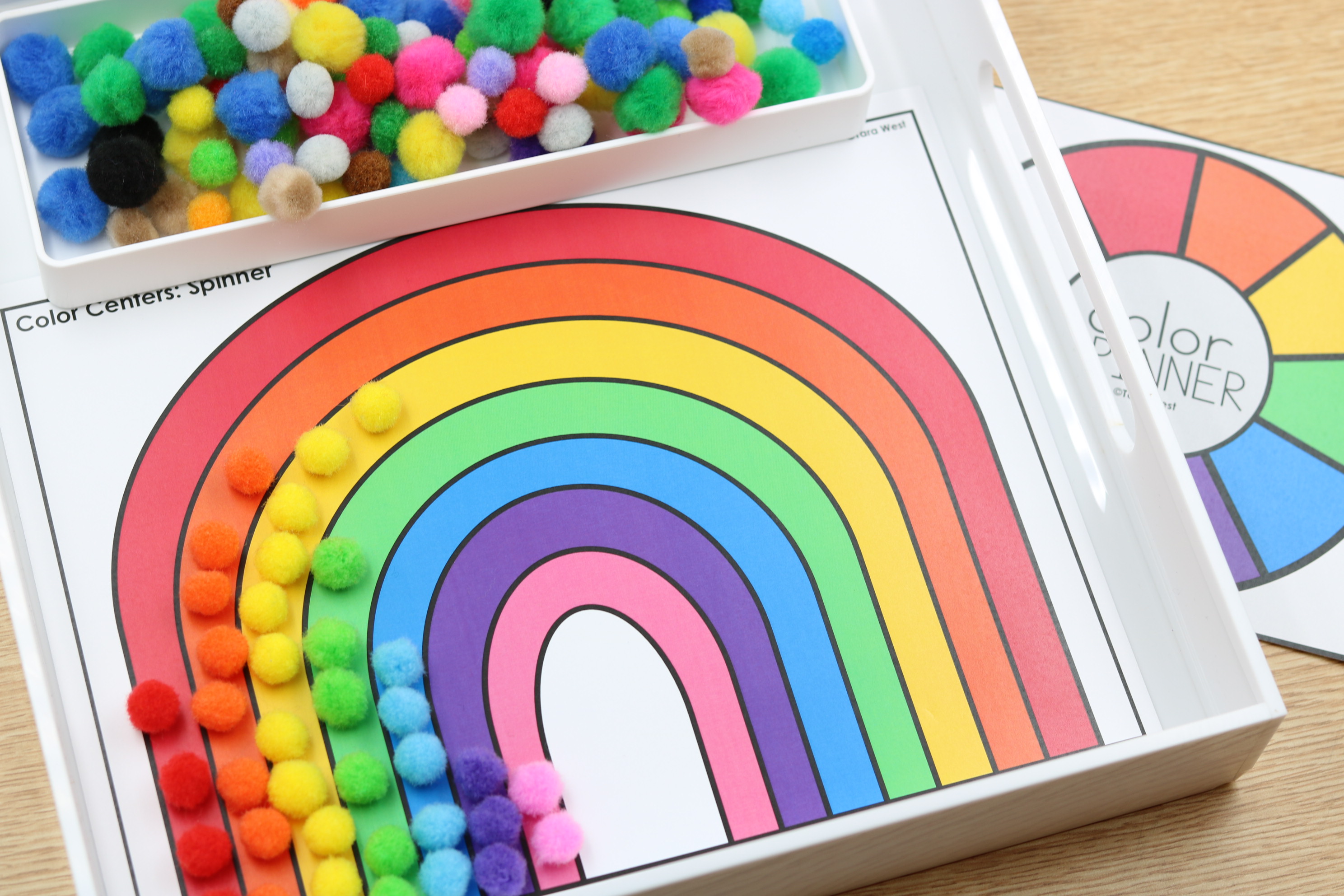 Rainbow fine motor alphabet center featuring colorful pom-poms placed along a rainbow mat for hands-on color matching and fine motor practice.