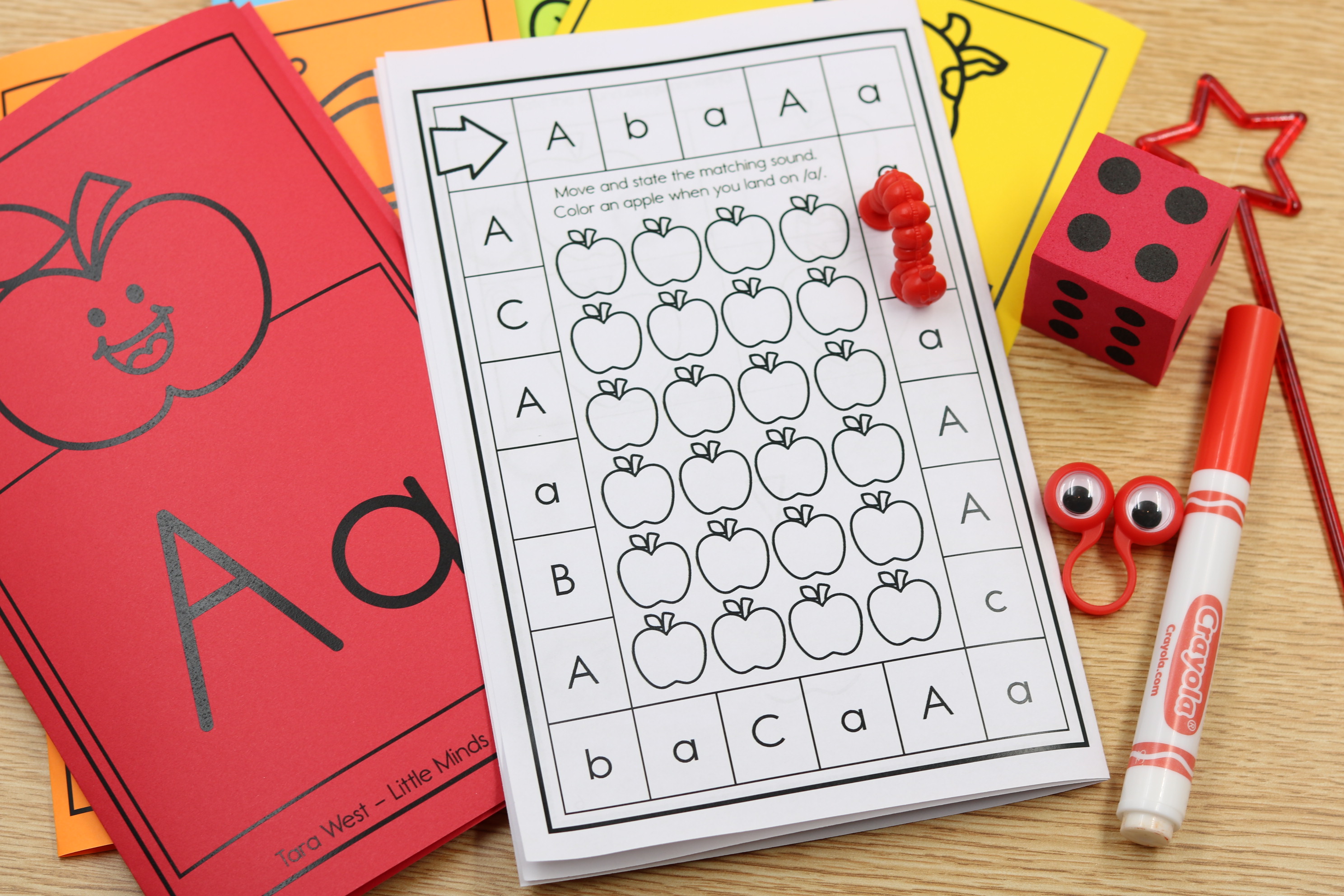 Back-to-school alphabet phonics center featuring an apple-themed letter A game board with uppercase and lowercase letter recognition, beginning sound practice, dice, and manipulatives.